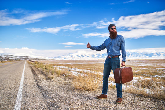 bearded hitch hiker thumbing for a ride on an empty nevada road