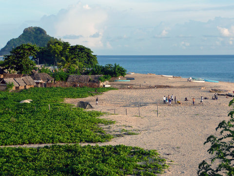 Fin de journ&eacute;e sur la plage d'un village africain des Comores. Les barques de p&ecirc;che sont renvers&eacute;es sur le sable, quelques personnes discutent, &agrave; l'arri&egrave;re-plan les premi&egrave;res maisons du village