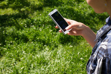 Woman holding smart phone in hand against green spring background. Blank screen with copyspace