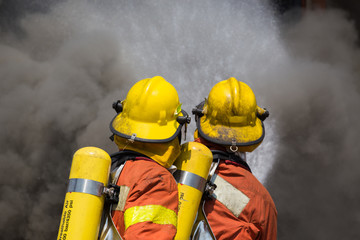 two firefighter in fire fighting suit spray water to fire and bl