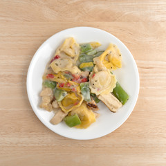 Chicken and tortellini TV dinner on a white plate atop a wood table.