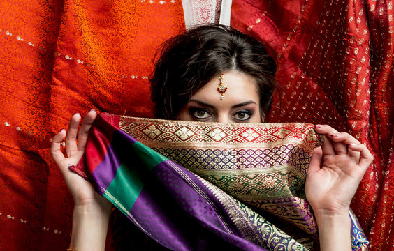 The young dark-haired woman hides a face behind a piece of colorful Indian saris. Indian style.