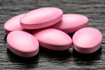 Pink pills (vitamins) on black background.