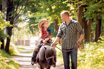 Beautiful little girl on a pony with his father
