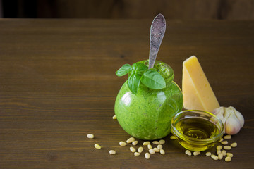 Homemade pesto sauce in a jar with ingredients over wooden table.