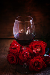 Red wine and red roses, black background, selective focus