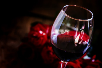 Red wine and red roses, black background, selective focus