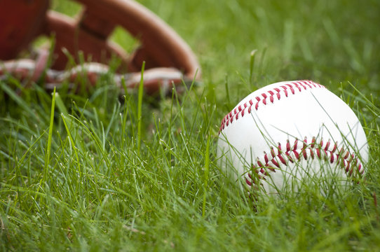 Photo of an Baseball ball and glove on green grass. Outdoor scene