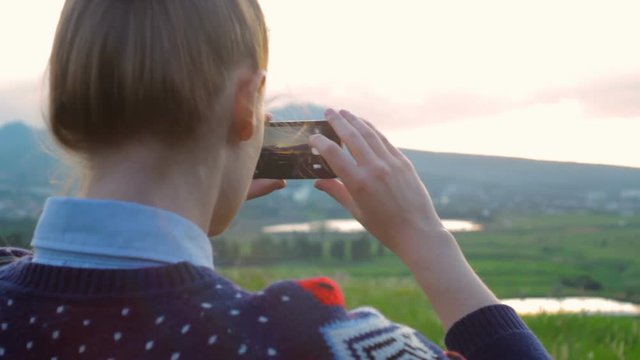 Young Attractive Woman Watching Sunset or Sunrise Over Bay from Top of the Mountain and Taking Panorama Photos on Phone.
