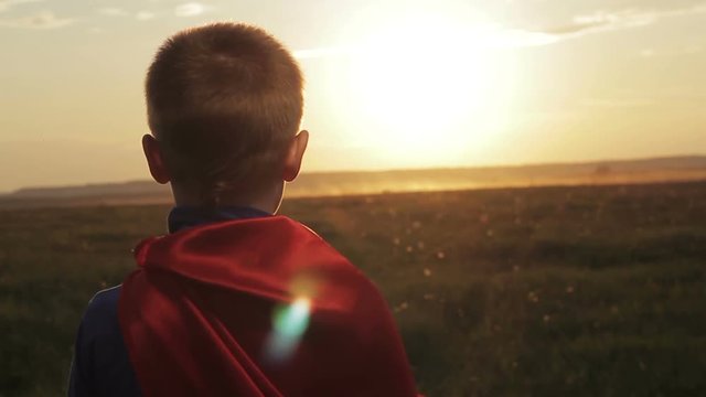 Boy dressed with a Superman cape running in a field, looking into the sunset