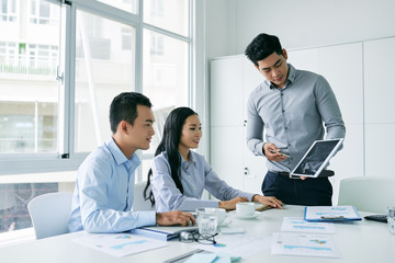 Young Asian businessman showing presentation on tablet computer to investors