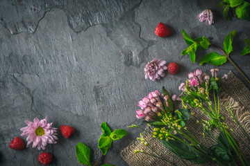 Flowers  , raspberries and mint on the dark stone background