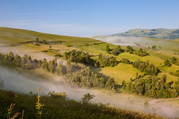 Fototapeta premium Colorful morning mist up the hills in the Romanian Apuseni Mountains near Salciua.