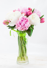 Summer bouquet of peonies in a glass vase on a white wooden tabl