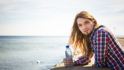 Fototapeta na wymiar Man long hair relaxing by seaside drinking water