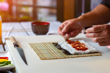 Spoon putting sauce onto rice. Man's hand holding small spoon. Tomato sauce for sushi filling. Proven recipe of tasty dinner.