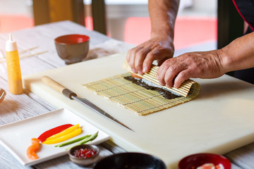 Man's hands touching bamboo mat. Knife lying near bamboo mat. Sushi chef in restaurant kitchen. Old recipe of futomaki rolls.