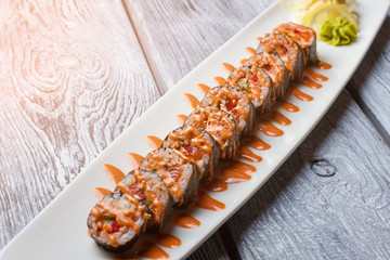 White plate with sushi rolls. Sauce of orange color. Meal served at sushi cafe. Recently cooked futomaki rolls.