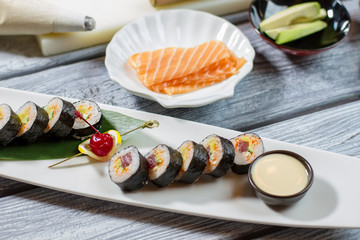 Fototapeta na wymiar Bowl with sauce beside sushi. Sushi rolls and sliced fish. Decorated plate with futomaki rolls. Proven recipe from japanese cuisine.