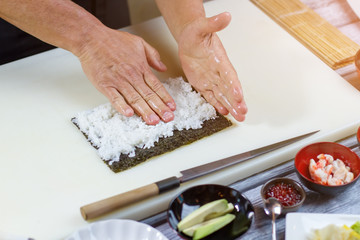 Hands touching white rice. Nori leaf beside a knife. Boiled rice for uramaki rolls. Sushi chef working in kitchen.