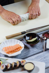 Man's hand touches sushi roll. Knife beside piece of avocado. Chef demonstrates the new recipe. Secrets of Japanese cuisine.