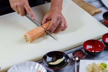 Hand holding knife cuts sushi. Thick sushi roll. Sushi chef cooks dinner. Proven recipe of japanese cuisine.