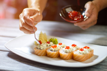 Spoon with caviar over sushi. Man's hand holding small spoon. Cream cheese and salmon caviar. Best recipe of uramaki rolls.