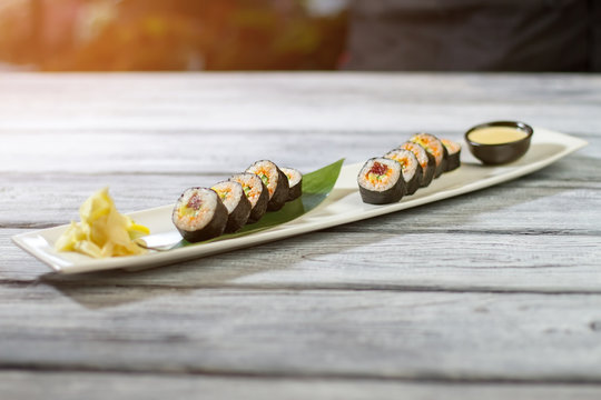 Sushi rolls on bamboo leaf. Long white plate with sushi. Futomaki rolls with special sauce. Tasty food low on calories.