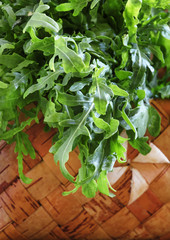 Bunch of fresh arugula in a wicker basket on an old wooden table