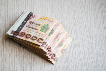Stack of thousand bath Thai money on wooden table with copy space