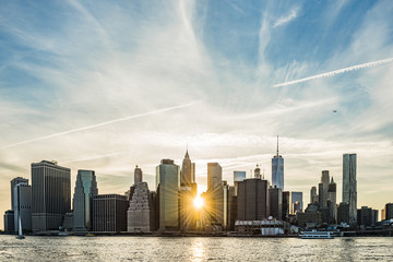 Sunburst between buildings of the Manhattan skyline in New York City during sunset with airplane