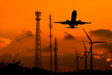 Silhouette telecommunications antenna, wind turbine and fly plane at sunset