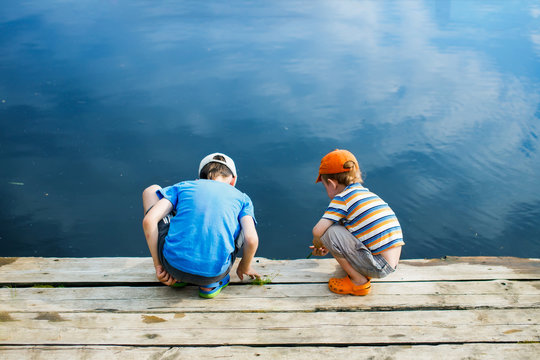 children play near the river. two boys looking into the water from the wooden pier. view from the back. safety concept