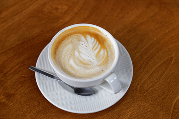 White cup of coffee cappuccino with pattern on foam cap on brown wooden table. Shallow focus.