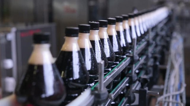 Soda, beer, carbonated drink pouring, filling, loading in to bottles on fresh drinks automated conveyor line.