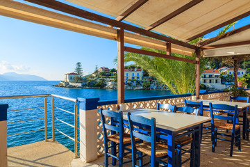 Blue chairs with tables in traditional Greek tavern in Fiskardo port, Kefalonia island, Greece - obrazy, fototapety, plakaty