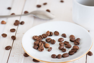 scattering coffee beans on a saucer cup and spoon in the background blur wooden surface