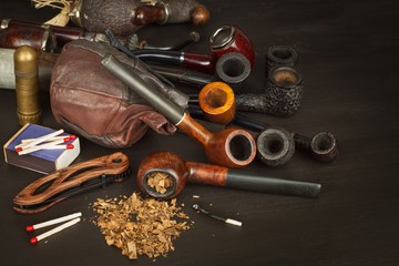 Old tobacco pipe and spilled tobacco, used on a black wooden background. Shabby old tobacco pipe. Wooden tobacco pipe on a black background. Relaxing with a tobacco pipe. Quiet place. Chain smoker.
