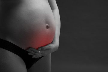 Caucasian pregnant woman in black lingerie with abdominal pain on gray studio background with copy...