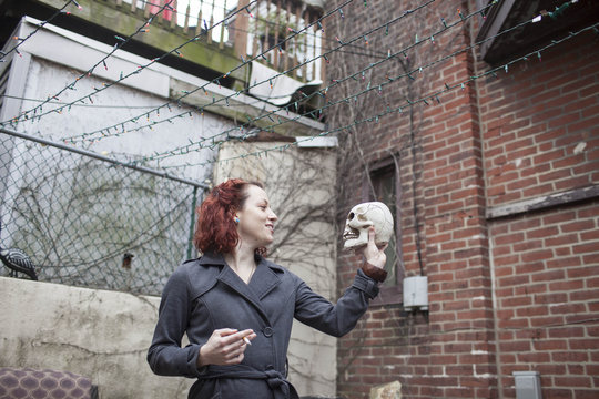 Young woman smoking cigarette while holding skull in hand
