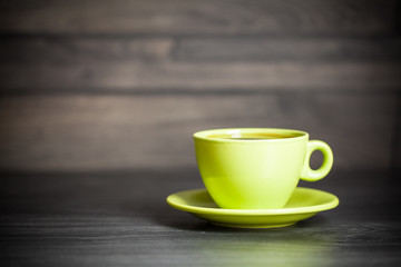 Green cup of hot tea on wood background with leaf. Autumn.
