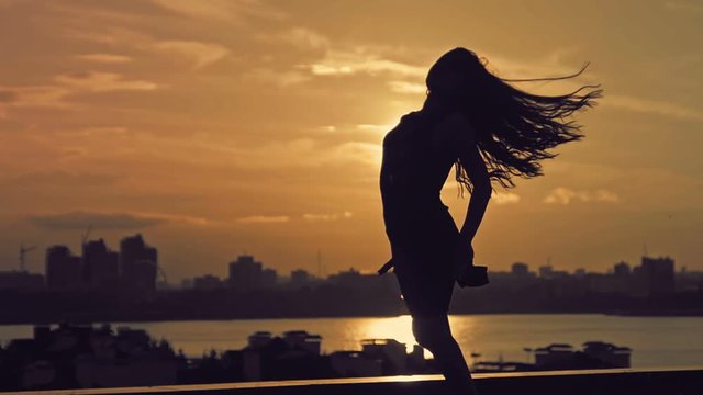 Young attractive girl with flowing hair doing the dance moves at sunset silhouette