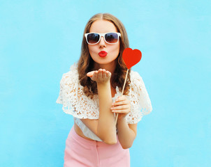 Pretty woman in sunglasses with red heart lollipop sends an air
