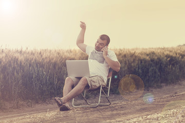 Businessman sitting in the field and working on laptop.