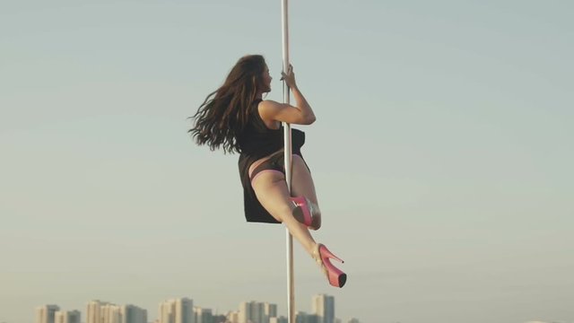 Fit attractive girl poledancer hanging on the pole at summer day on portable dancing stage over the skyline