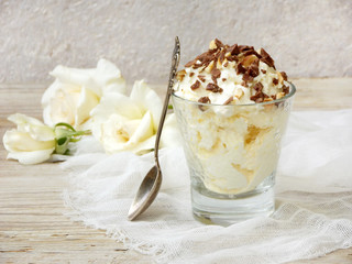 Homemade butter or lemon ice cream sprinkled with nuts and chocolate in a glass on a light wooden background with white roses