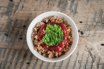 Buckwheat porridge with tomato sauce and leaf salad in a white bowl on a wooden table next to a ceramic bowl with dish is carrots or sliced carrot. Food background. Nice and tasty atmosphere.