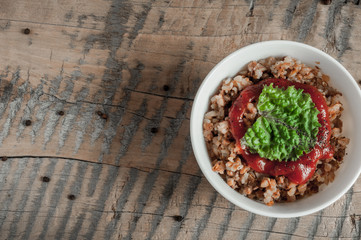 Buckwheat porridge with tomato sauce and leaf salad in a white bowl on a wooden table next to a ceramic bowl with dish is carrots or sliced carrot. Food background. Nice and tasty atmosphere.