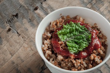 Buckwheat porridge with tomato sauce and leaf salad in a white bowl on a wooden table next to a ceramic bowl with dish is carrots or sliced carrot. Food background. Nice and tasty atmosphere.