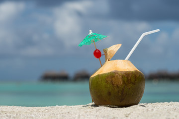 Coconut with drinking straw on beach at the sea